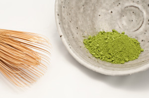 A bowl of green powder next to some bamboo sticks